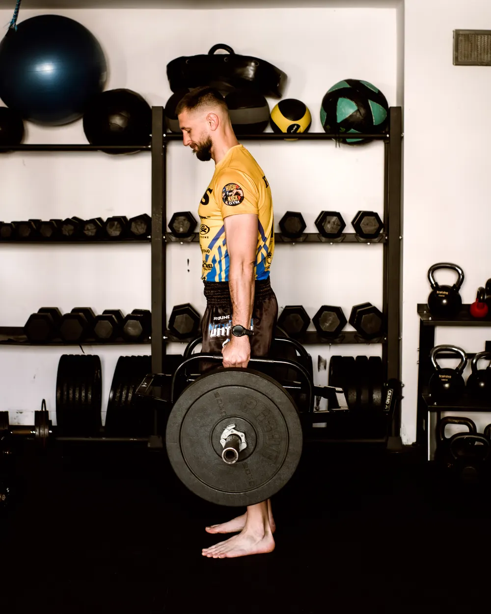 Marcin Kujawa z trap barem na tle regałów z hantlami i kettlebellami